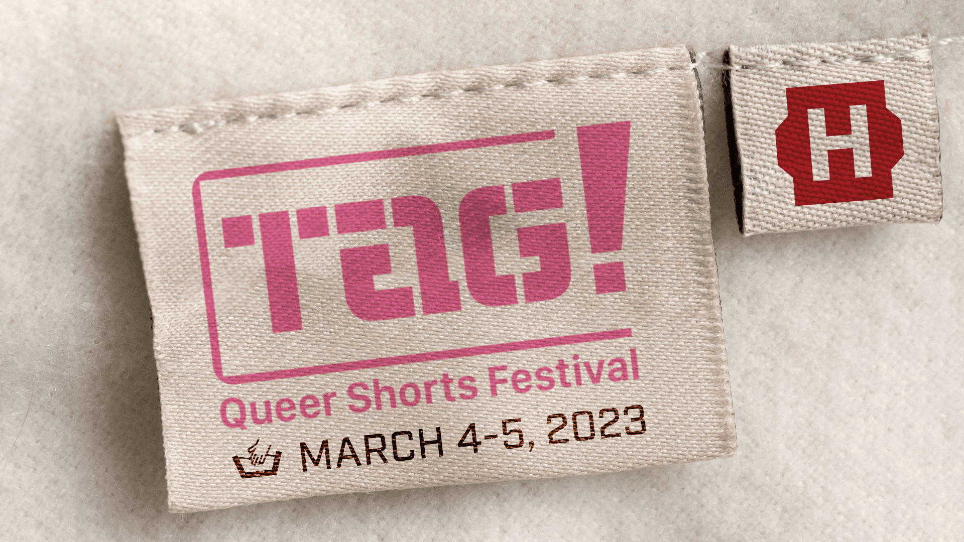 Clothing tag with the logo of the Tag Queer Shorts festival next to a second label with the Hollywood Theatre logo.