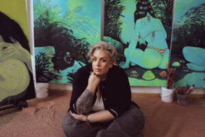 Artist, Raé Sheridan sits infront of one of her paintings.